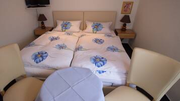 A neatly arranged bedroom with a bed, two bedside tables, a TV mounted on the wall, and two chairs.