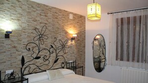 Een slaapkamer met een muur met baksteenpatroon, een bed met witte dekbedovertrek, een nachtkastje, een spiegel bevestigd aan de muur en een raam met gordijnen.