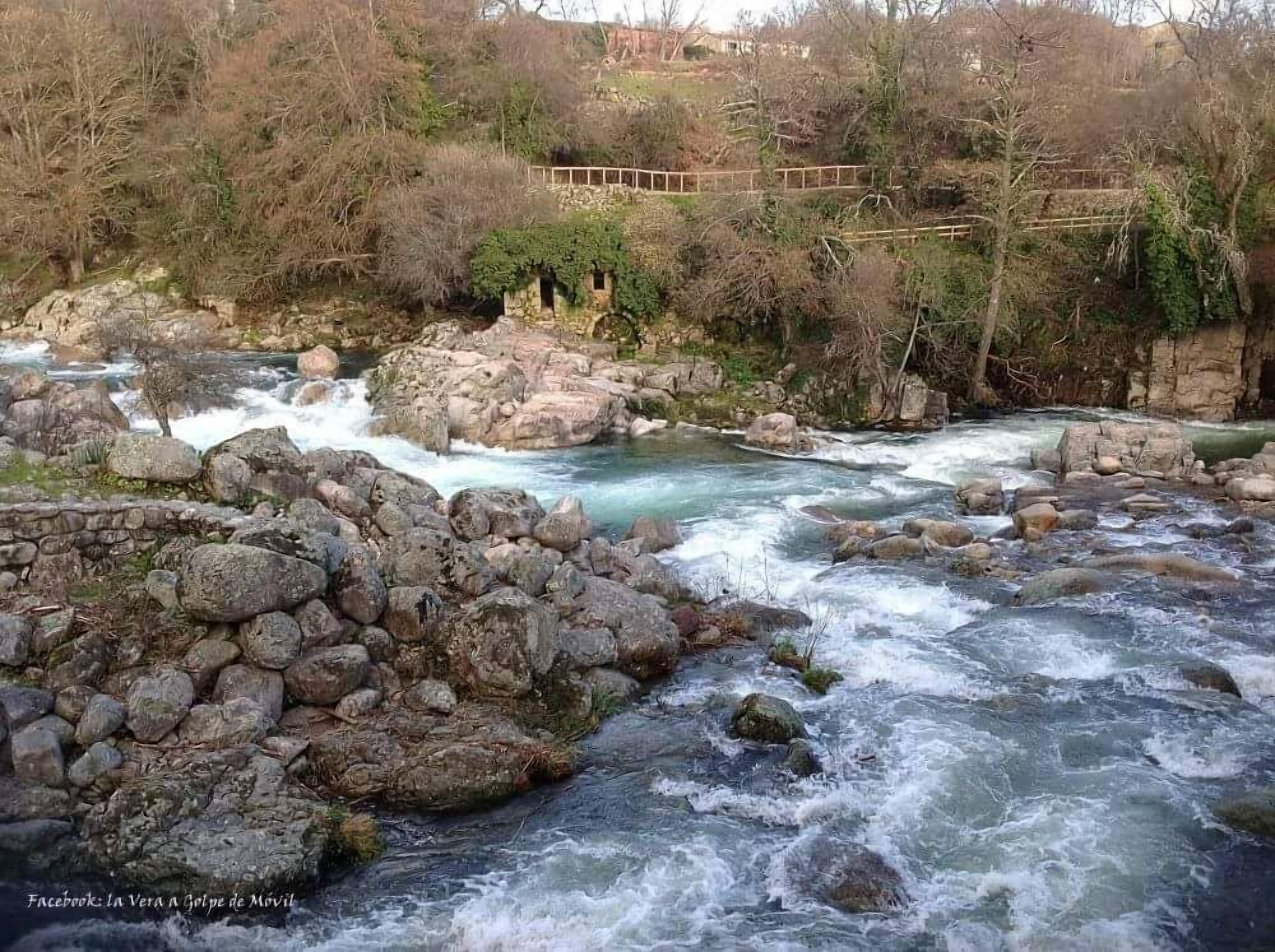A river flowing through a rocky landscape with a stone bridge in the background.