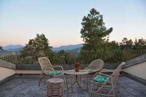 A terrace with wicker furniture, a small table with a potted plant, and a view of mountains and trees. - Ca' Lavalle B&B (Urbino)