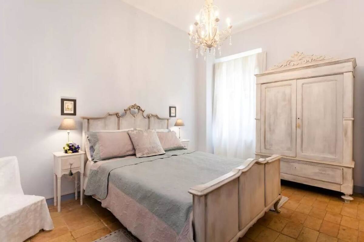 A bedroom with a bed, nightstands, a dresser, and a chandelier.