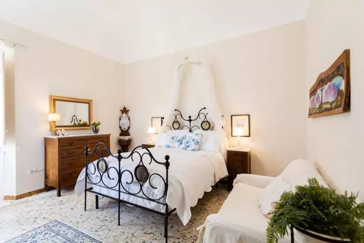 A bedroom with a bed, bedside tables, a dresser, a mirror, and a painting on the wall.