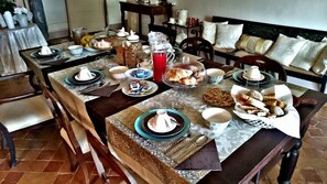 Un comedor con una larga mesa dispuesta para el desayuno, que incluye platos, tazas y una variedad de pasteles y pan.