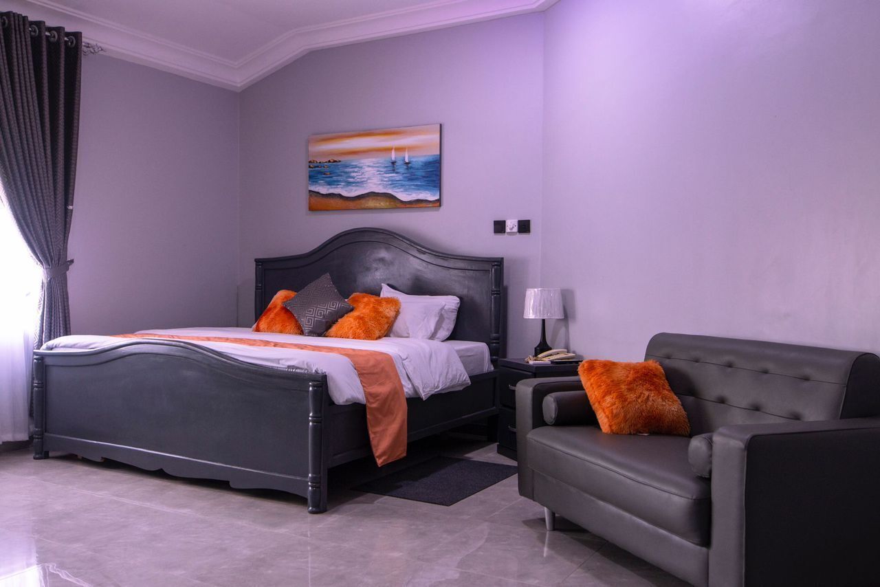 A bedroom with a bed, a nightstand, a lamp, and a sofa.