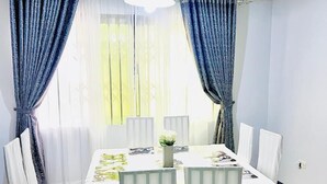 A dining room with a rectangular table set for six, surrounded by white chairs with white covers. - KCS Guest House (Accra)