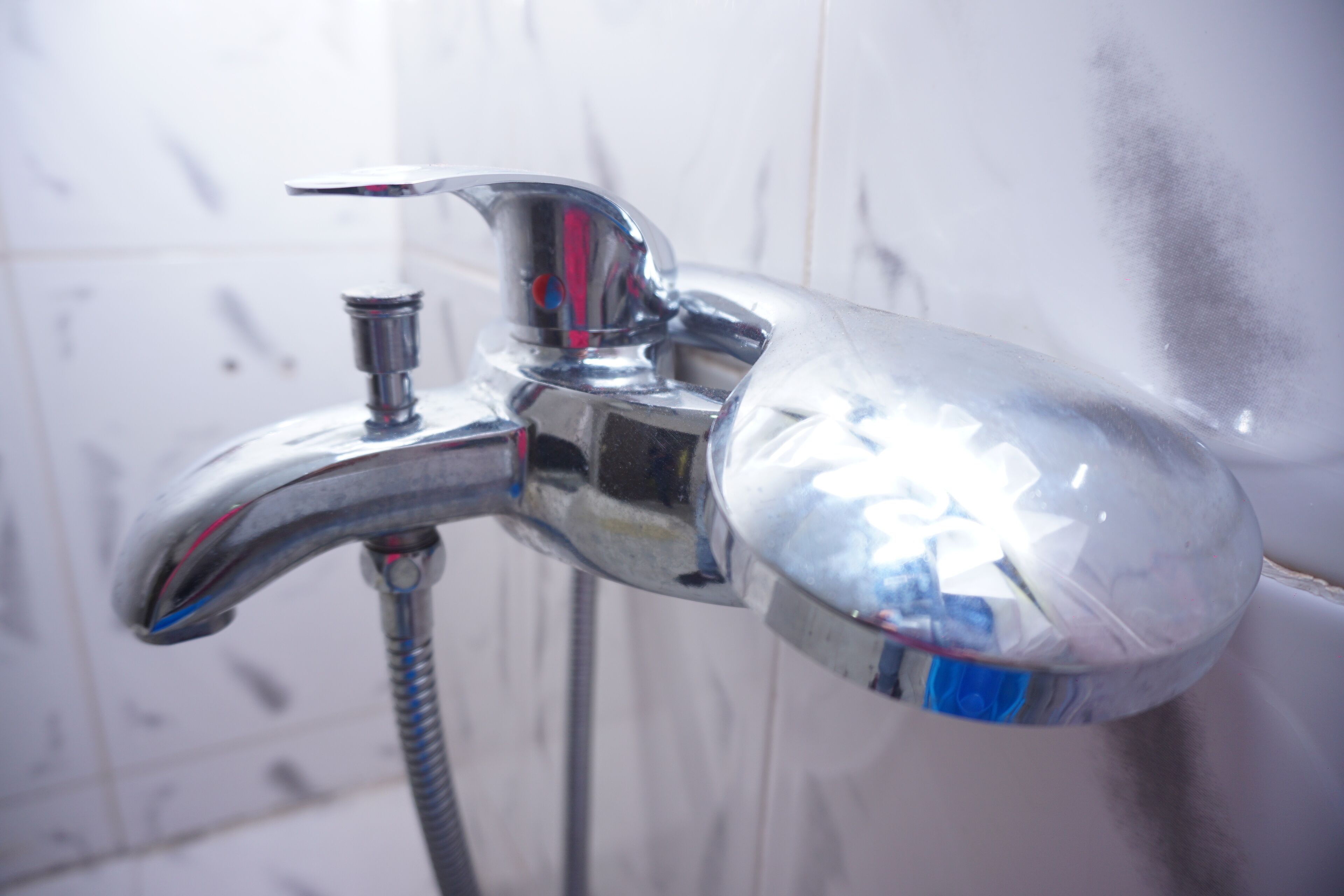 A chrome faucet with a flexible hose, attached to a white tiled wall.