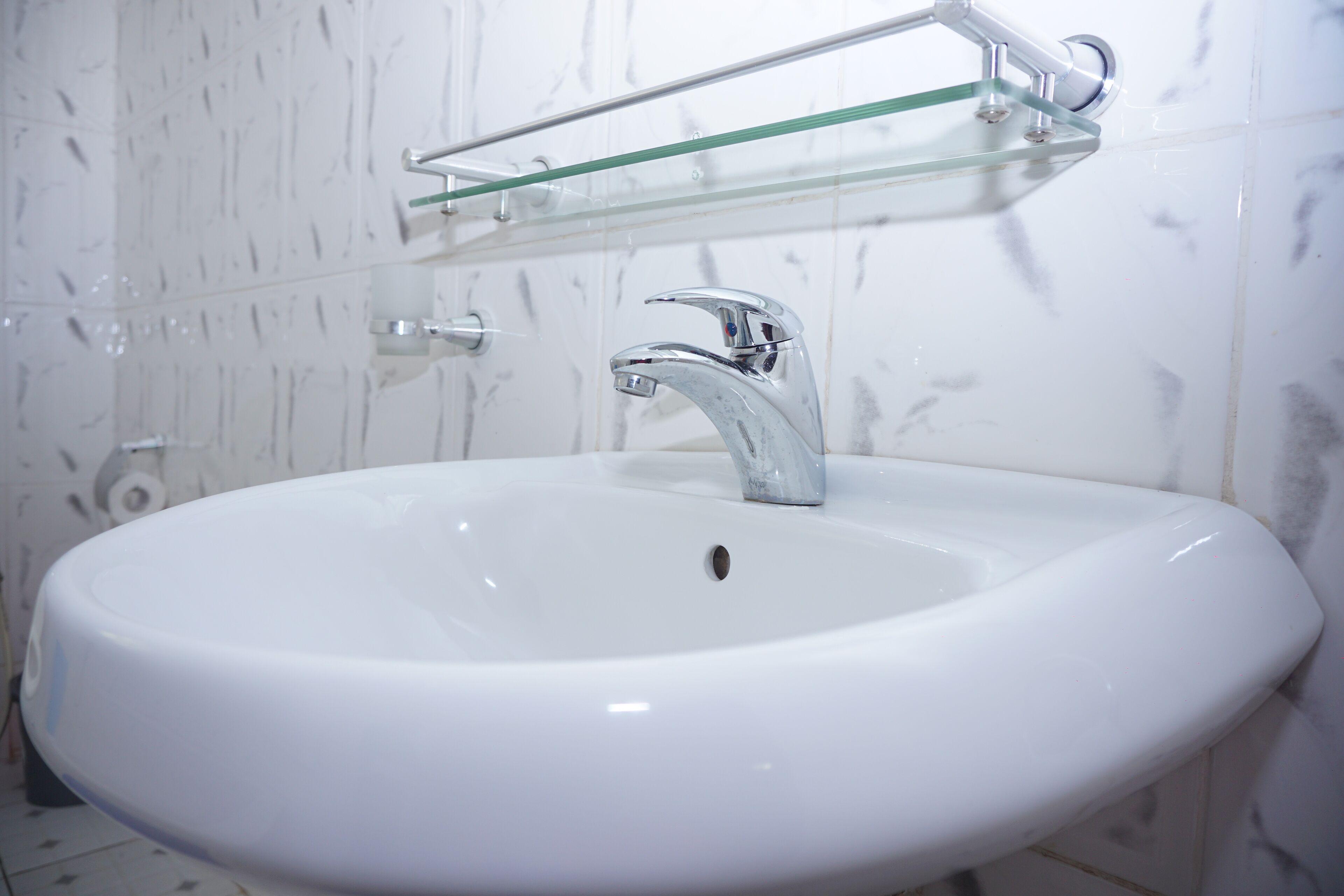 Un lavabo blanc pour la salle de bain, doté d’un robinet chromé et d’une étagère en verre au-dessus.