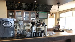 Un comptoir de café avec une machine à café, un tableau noir affichant le menu et des ustensiles de cuisine.