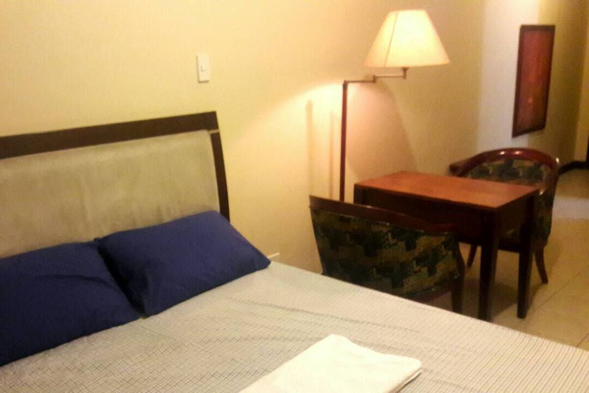 Un lit avec deux oreillers, une table de chevet, une chaise et une lampe.