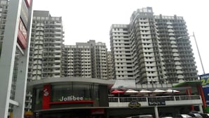 Un restaurant Jollibee au design moderne, situé dans un quartier commercial, avec de grands immeubles en arrière-plan.