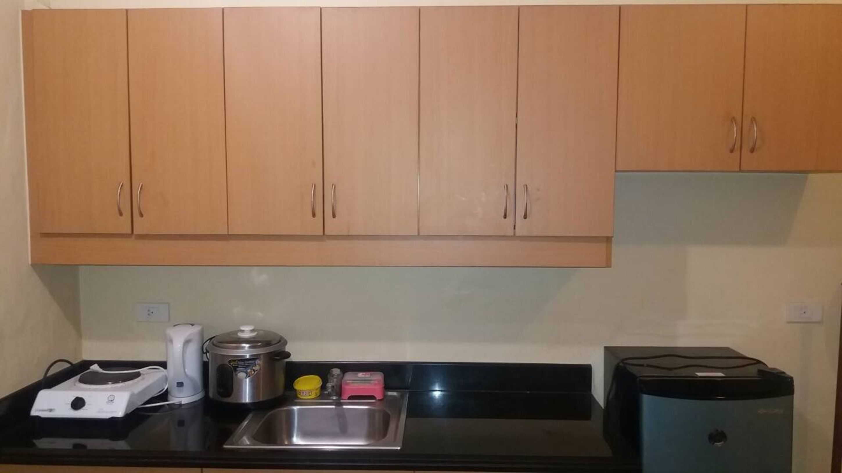 A kitchen with wooden cabinets, a stainless steel sink, a coffee maker, a rice cooker, and a blender.