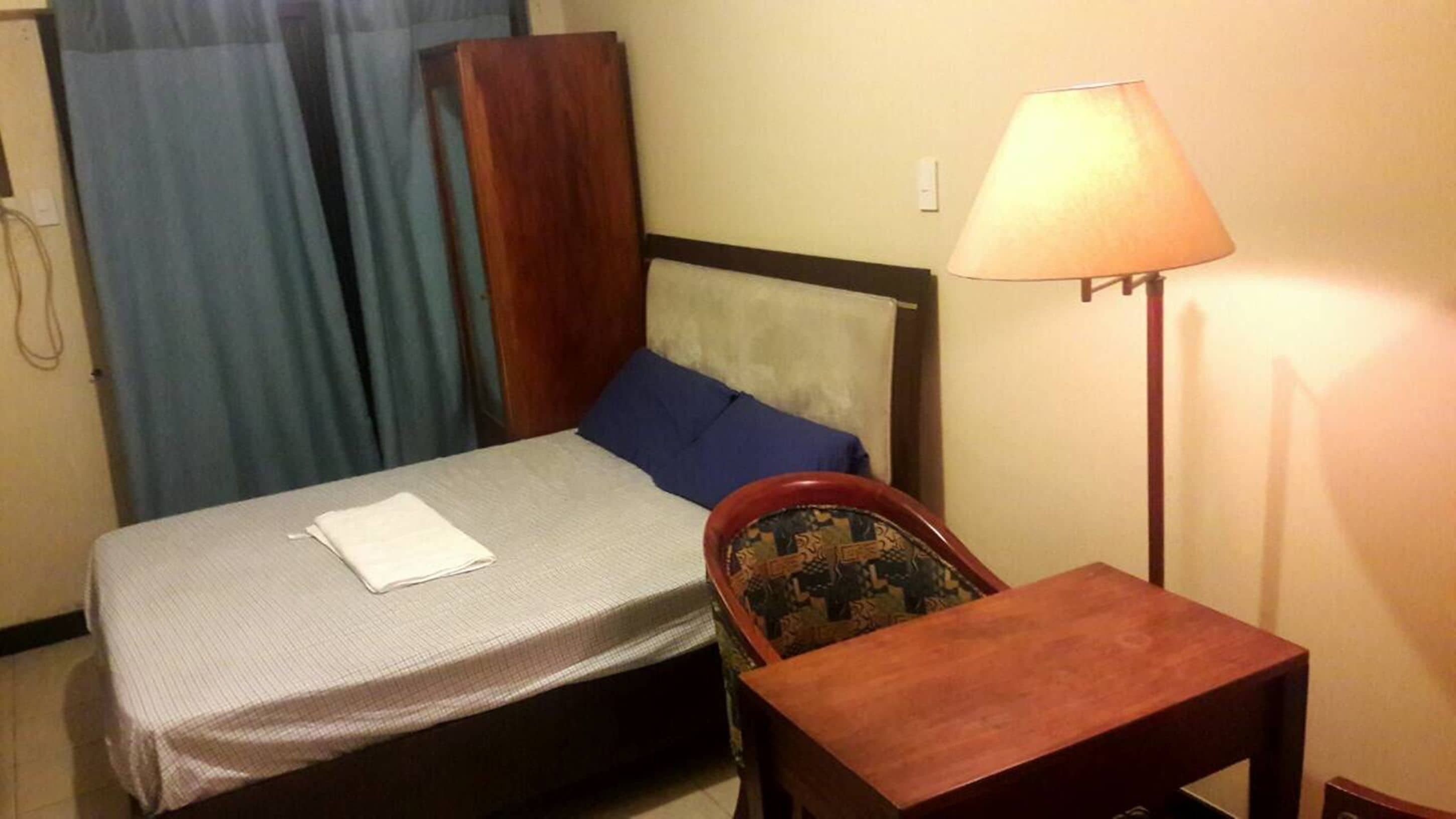 Una habitación de hotel con cama, una silla, una mesa, una lámpara y cortinas.