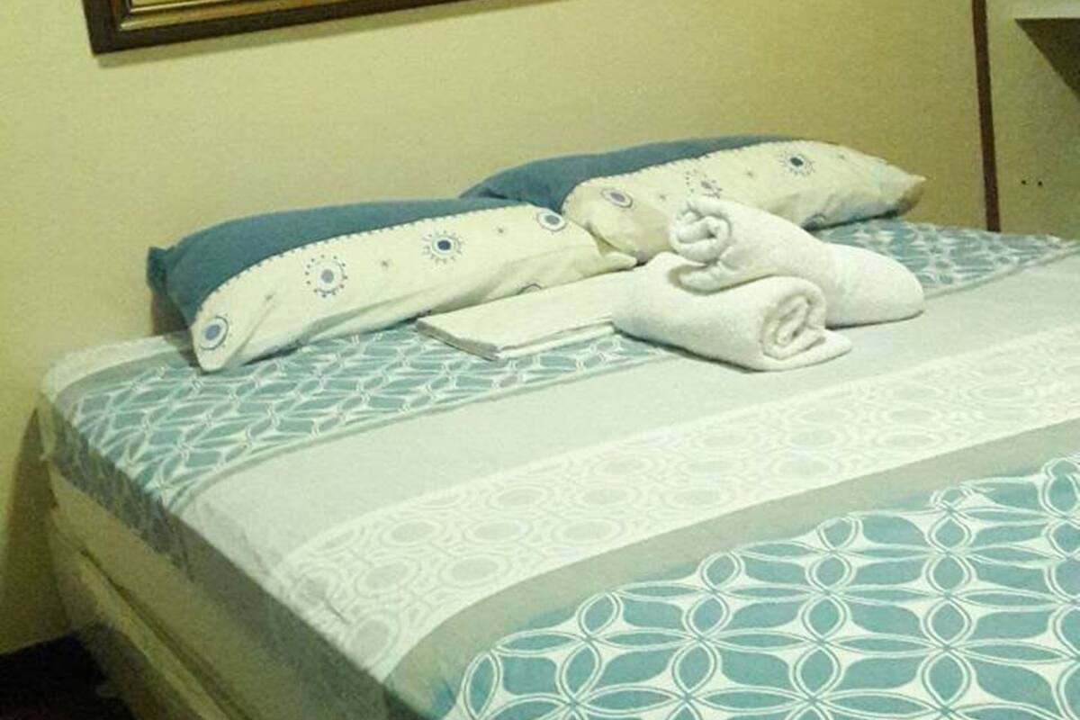 Un lit bien fait, avec une couvre-lit à motifs, un oreiller et une serviette pliée.