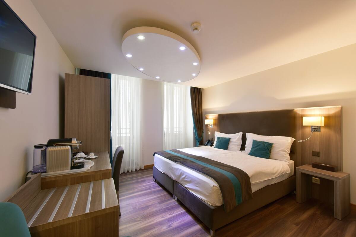 Una camera d'albergo con un letto grande, una scrivania, una sedia, una TV e un lampadario.