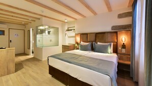 Une chambre d’hôtel avec un plafond en bois, un grand lit avec une tête de lit, des tables de chevet avec des lampes, un miroir et une armoire.