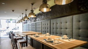 L'intérieur d'un restaurant avec des tables en bois, des banquettes rembourrées et des luminaires suspendus.