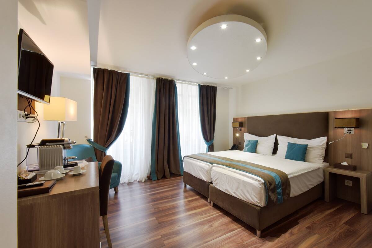 Una camera d'albergo con un letto, comodino, lampada, scrivania e sedia, e televisore.