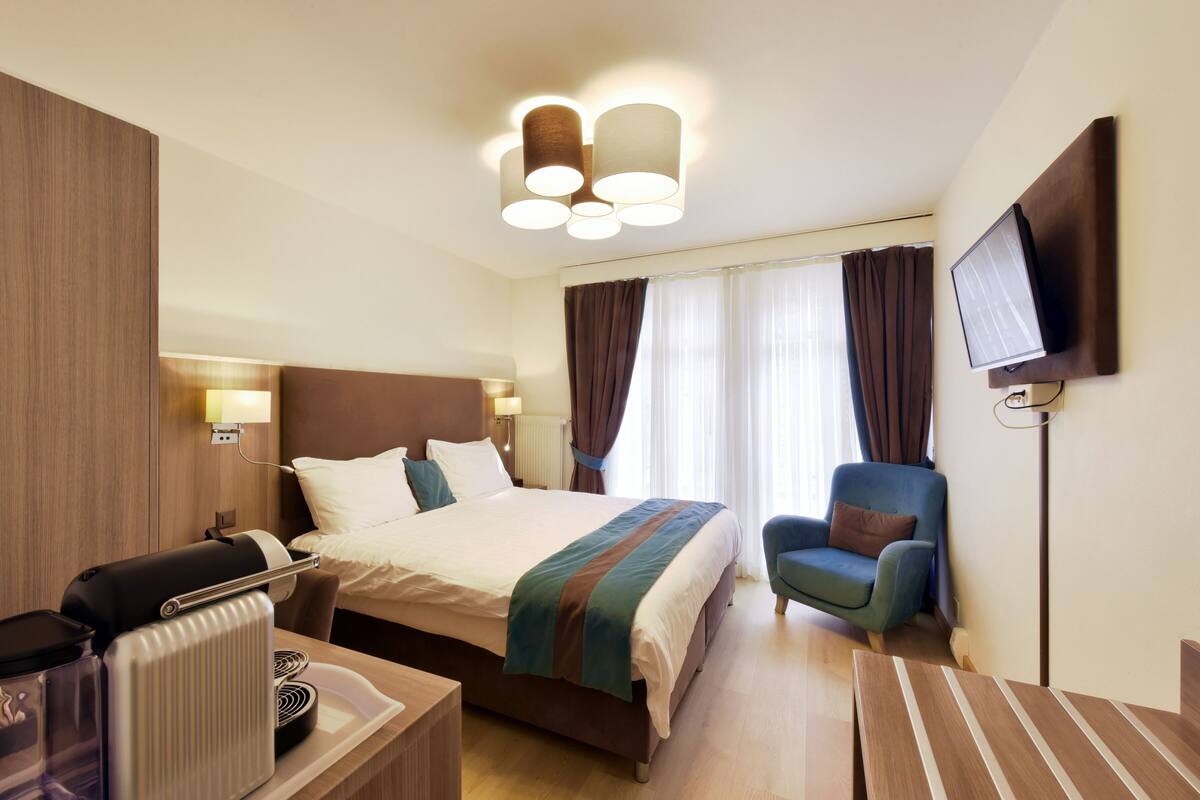 Una camera d'albergo con un letto grande, una scrivania con un computer, una sedia e una TV a schermo piatto fissata al muro.