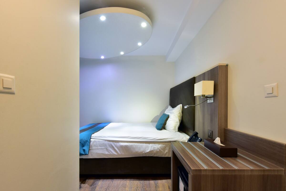 Una camera d'albergo con un letto, comodino, lampada e una moderna lampada a sospensione.