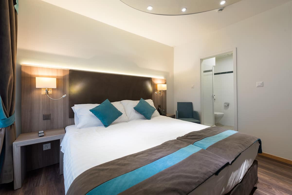 Una camera d'albergo moderna con un letto grande, lampade ai comodini, uno specchio e una porta.
