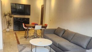 Una sala moderna con un sofá seccional gris, una mesita de centro blanca y un televisor de pantalla plana montado en la pared.