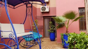 Un patio con una silla mecedora, plantas en macetas y un aire acondicionado de pared.