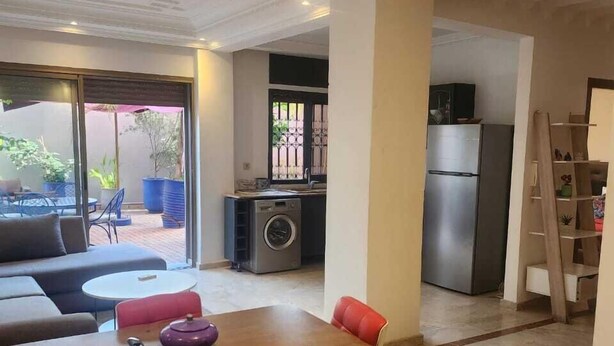 Cocina moderna con refrigerador, estufa y lavadora. Cuenta con un comedor con mesa y sillas, y una pequeña sala de estar con sofá y sillas.