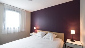 Habitación de hotel con una cama grande, dos mesitas de noche, una ventana con cortinas y una pared pintada de color oscuro.