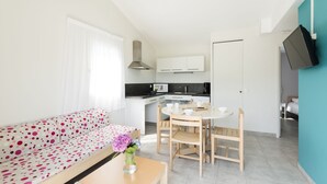 Una sala de estar moderna con sofá, una mesa de comedor con sillas, un área de cocina y un televisor montado en la pared.