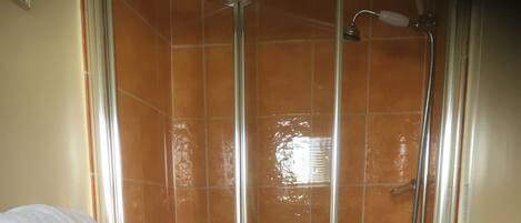 Una doccia con porta in vetro, pareti rivestite di piastrelle arancioni e nere, e un portasciugamani bianco.