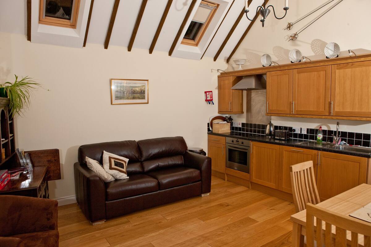A modern kitchen with wooden cabinets, a dining table, and a brown leather sofa.