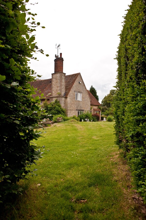 A stone house with a grassy yard, surrounded by dense foliage.