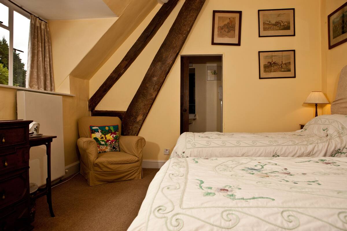 A bedroom with two beds, a chair, a dresser, and a window with curtains.