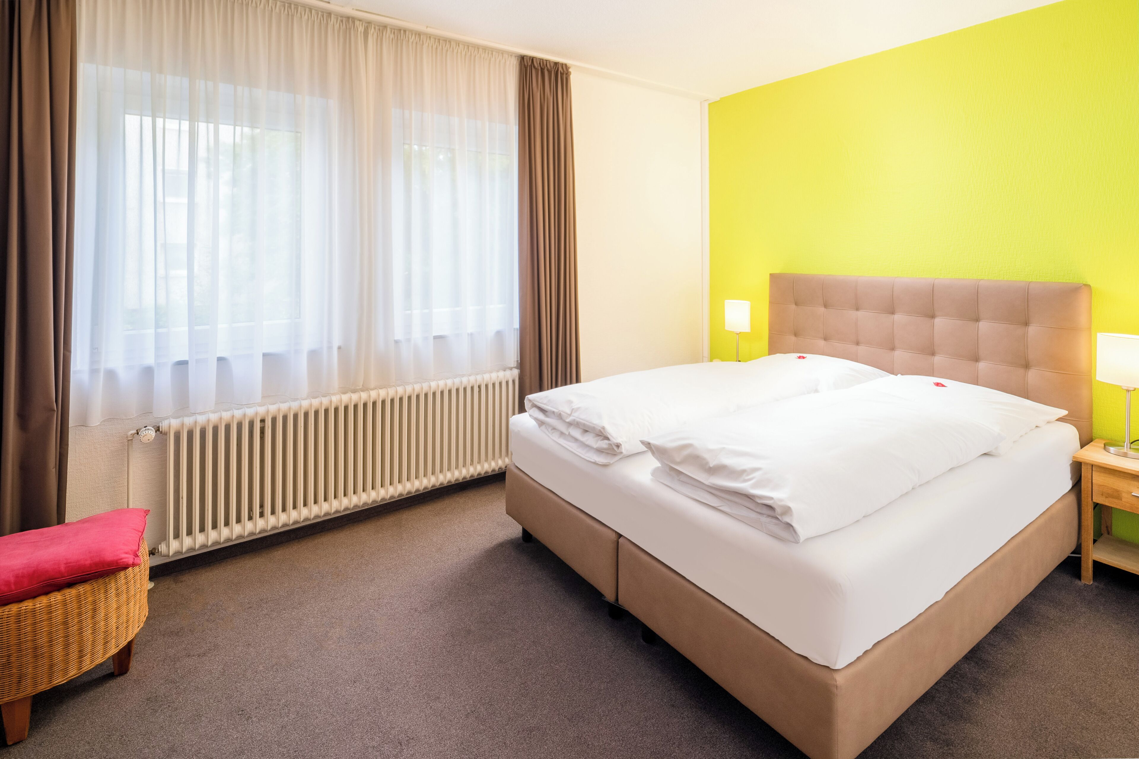 A hotel room with a bed, a chair, a nightstand, and a window with curtains.