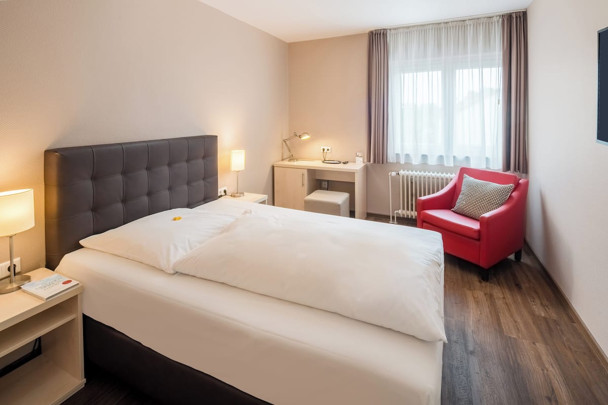 A hotel room with a bed, a desk, a chair, and a window with curtains.