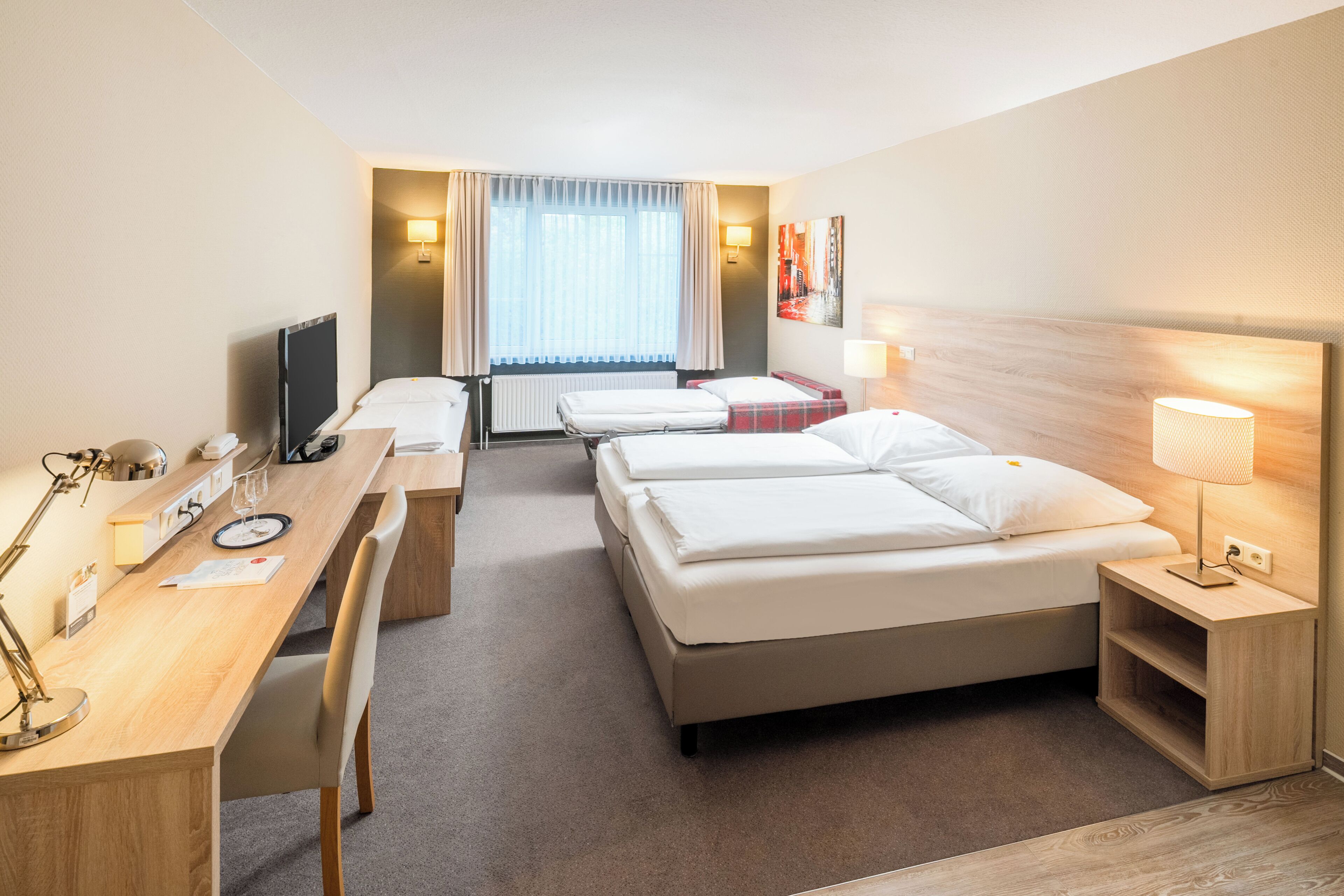 Ein Hotelzimmer mit Bett, Schreibtisch, Stuhl, Fernseher und Lampe.