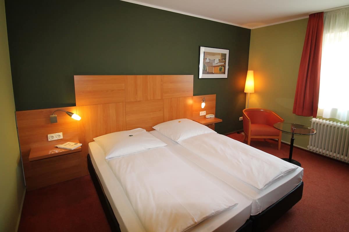 A hotel room with a bed, two bedside tables, a chair, a lamp, and a radiator.