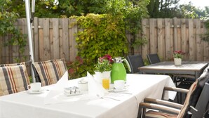 An outdoor dining area with tables set for breakfast, surrounded by a wooden fence and greenery. - Hotel Westerfeld (Hemmingen)