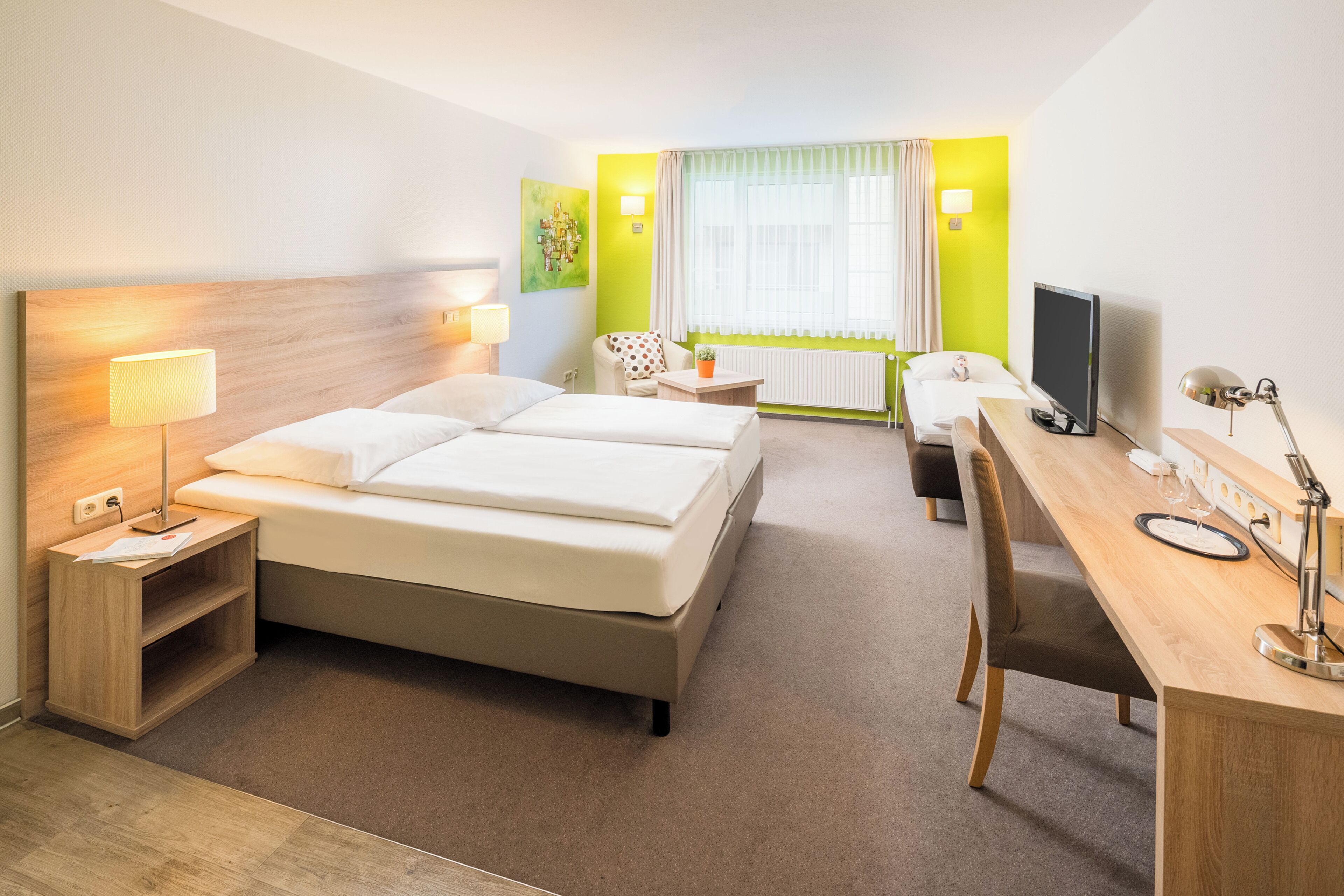 Habitación de hotel con cama, escritorio, silla, lámpara, televisión y ventana con cortinas.