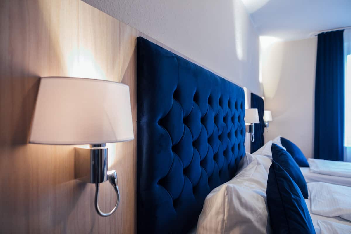 A hotel room with a tufted headboard, a bedside lamp, and a bed with blue pillows.