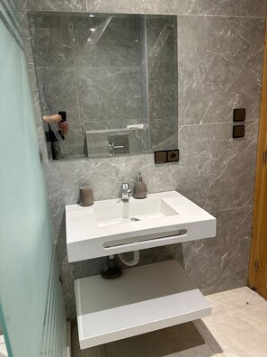 A modern bathroom with a white vanity, a large mirror, and marble walls. - Appartment Centre Gueliz (Marrakech)