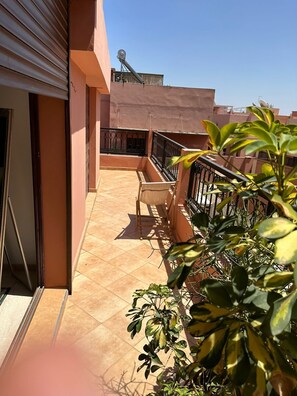 A balcony with a chair and a small table, a tiled floor, and a view of neighboring buildings. - Appartment Centre Gueliz (Marrakech)