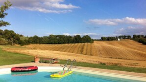 A swimming pool with inflatable toys, surrounded by a grassy area and a field of crops. - Agriturismo Fattoria Santa Vittoria (Foiano della Chiana)