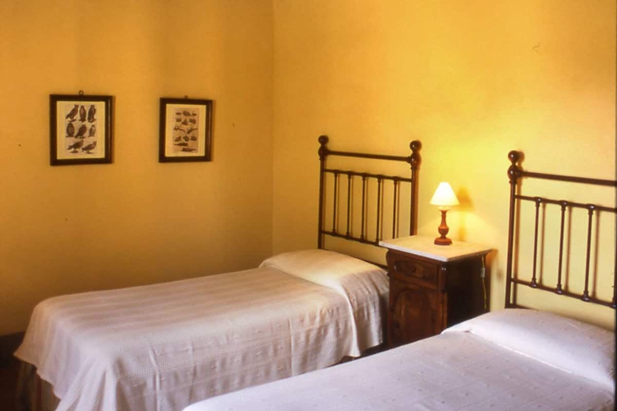 A room with two single beds, wooden beams on the ceiling, and two framed pictures on the wall.
