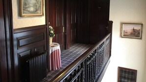 A hallway with a dark wooden door, a small table with a pink tablecloth, and a framed painting on the wall. - The Cowrie Guest House (Berwick-upon-Tweed)