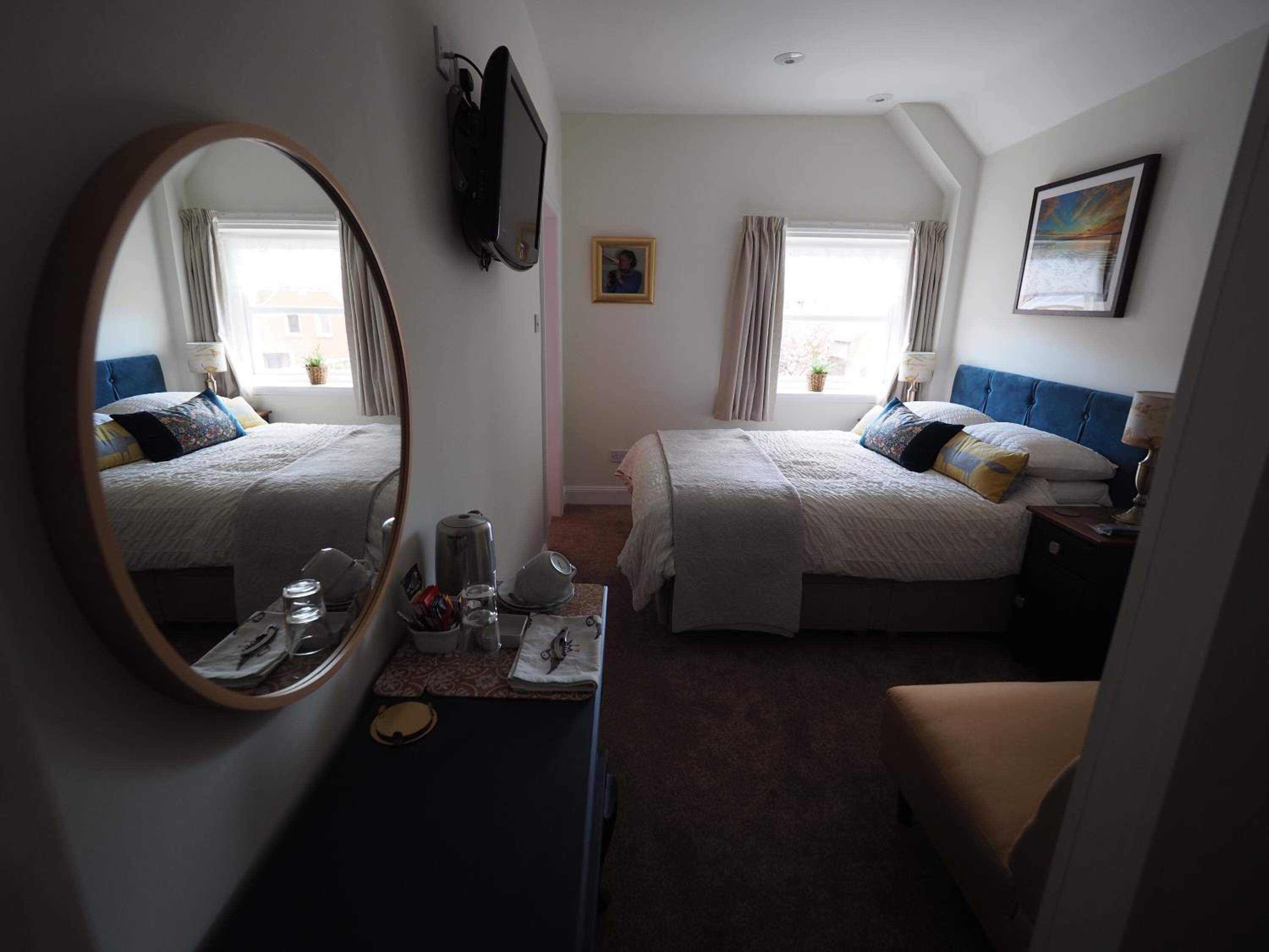Habitación de hotel con dos camas, un espejo grande, un escritorio con artículos de aseo y un cuadro en la pared.