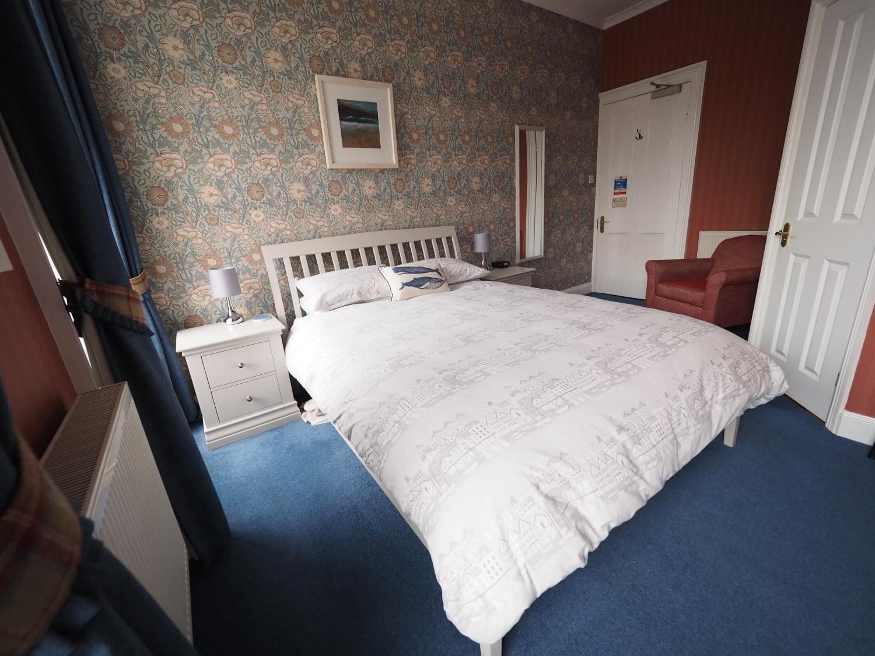 Een slaapkamer met een groot bed, een nachtkastje, een stoel en een deur.