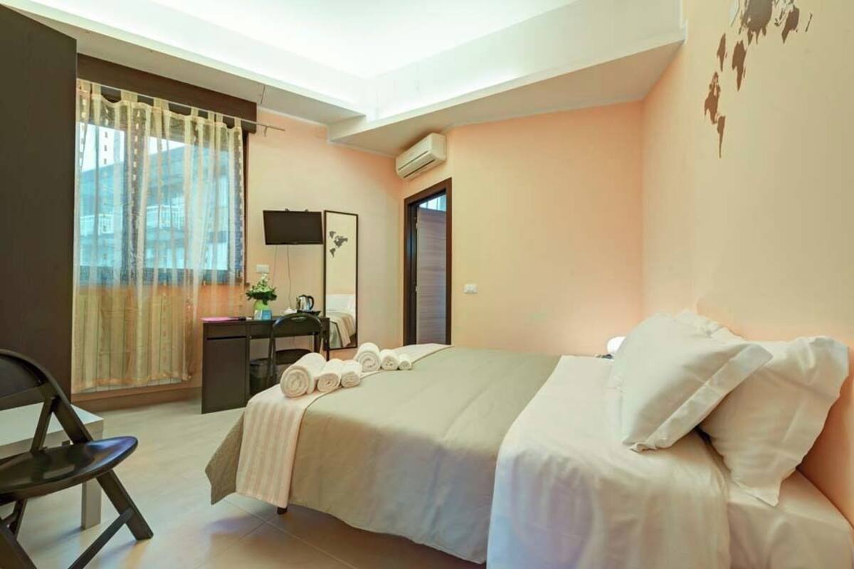 A hotel room with a bed, a desk, a chair, and a window with curtains.