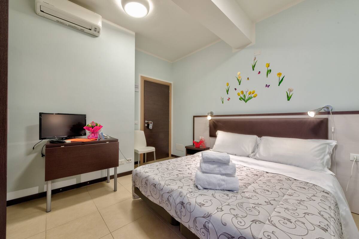 A hotel room with a bed, a desk with a computer, a TV, and a wall with flower decals.