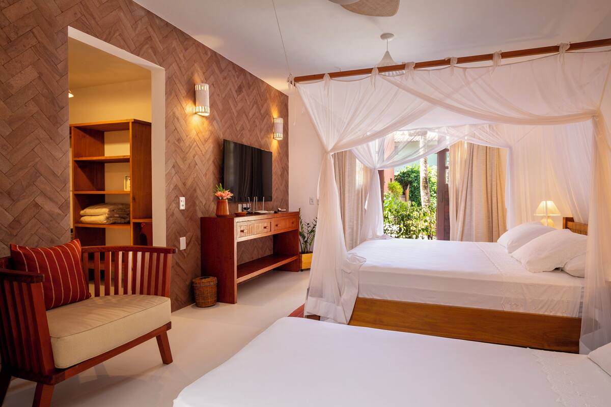A bedroom with a bed, a wooden bench, a TV, and a desk with a lamp.